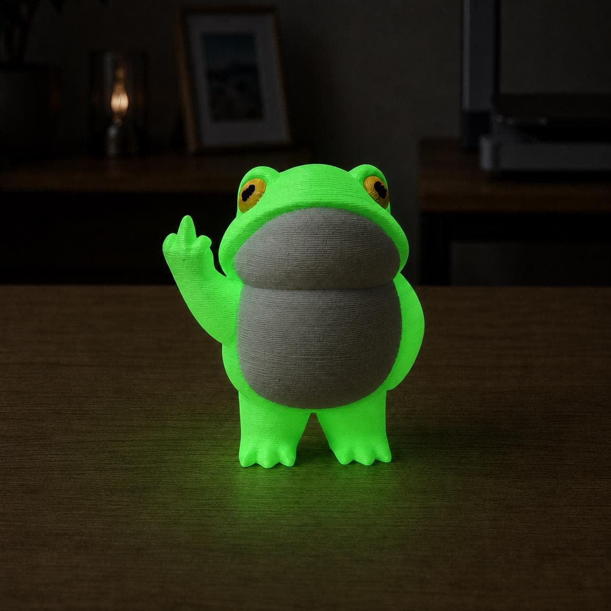 Glow-in-the-dark frog figurine shining bright green in a dark room, with a rounded belly and cheeky raised middle-finger gesture.
