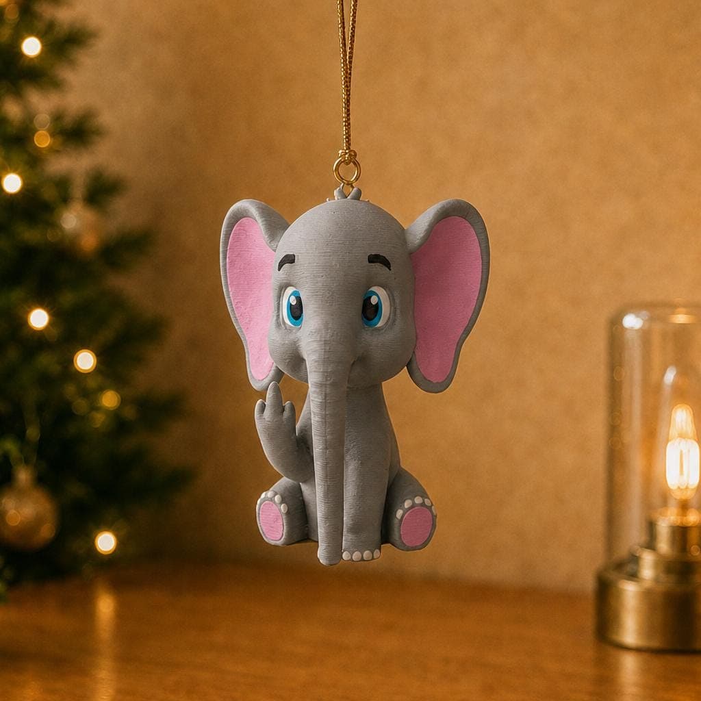 Cute baby elephant ornament hanging beside a decorated Christmas tree and warm lamp, with blue eyes, pink ears and a cheeky hand gesture.