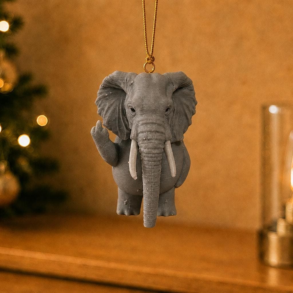 Funny grey elephant ornament hanging beside a decorated Christmas tree and warm lamp, with broad ears, white tusks and raised middle finger.