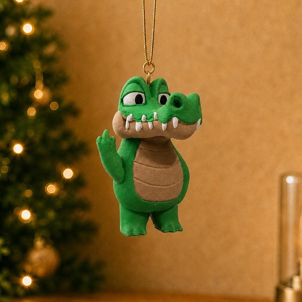 Funny green crocodile ornament hanging beside a decorated Christmas tree and warm lamp, with a tan belly and raised middle finger.