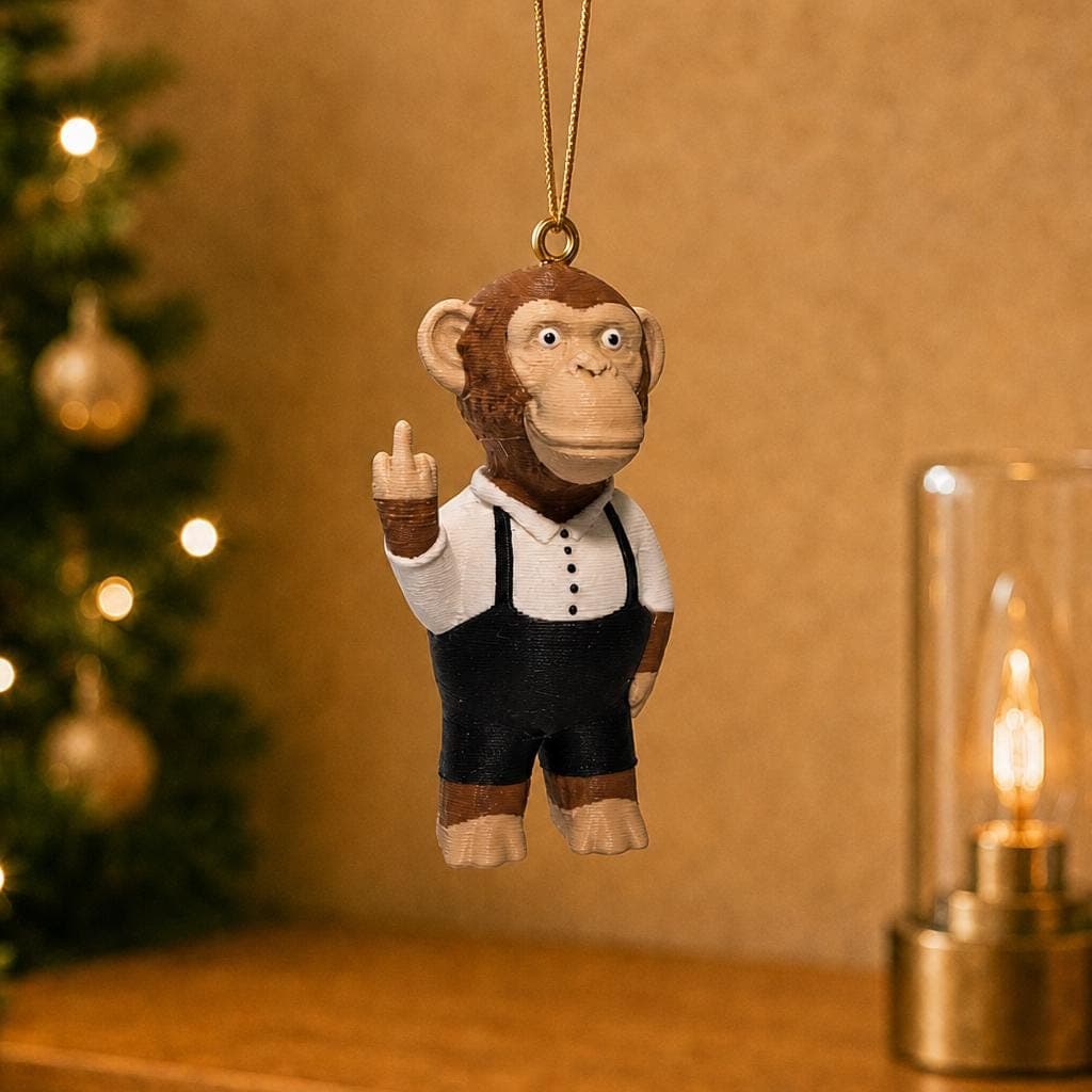 Funny monkey ornament hanging beside a decorated Christmas tree and warm lamp, wearing a white shirt, black suspenders and raising its middle finger.